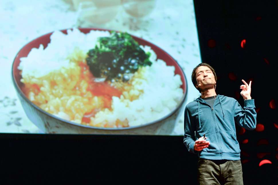 写真：卵かけご飯の映し出されたスクリーンを背にスピーチする荘司さん