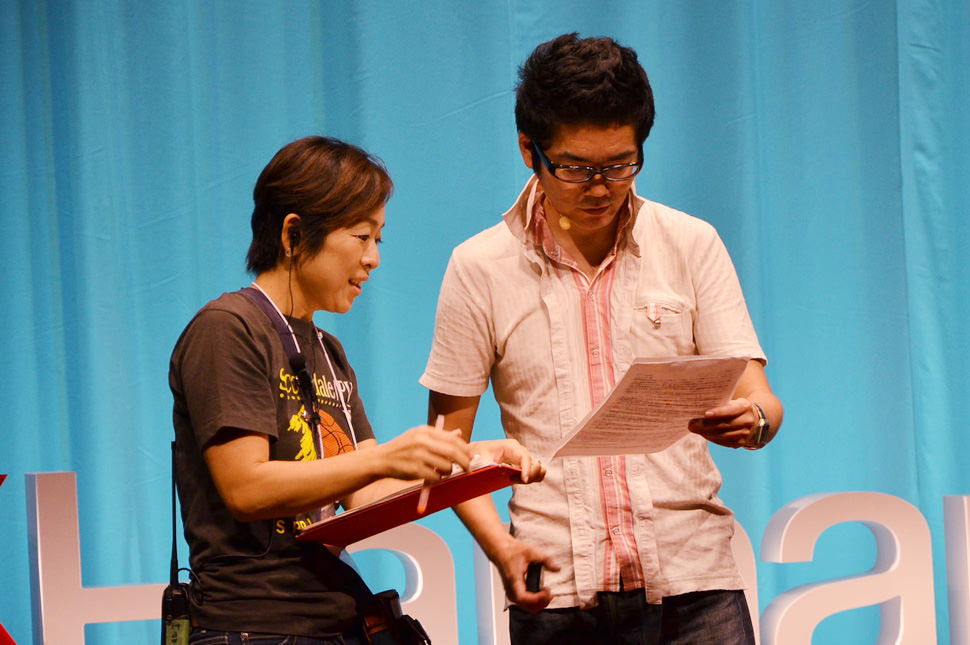 写真：ステージ上でスピーカー担当スタッフとトークのチェックをする杉山さん